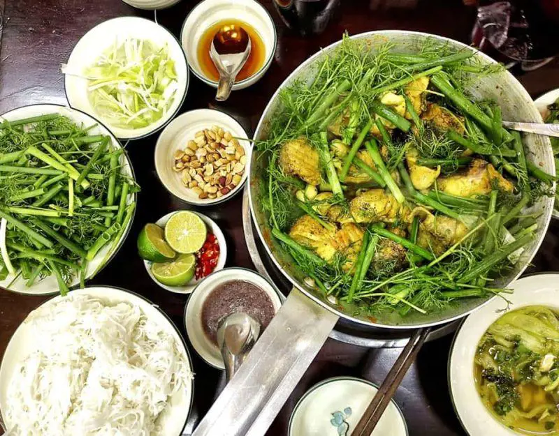 Chả Cá Lã Vọng với nhiều thì là và hành lá, ăn kèm bún trắng, lạc rang, mắm tôm, chanh, ớt và rau xanh trên bàn ăn.