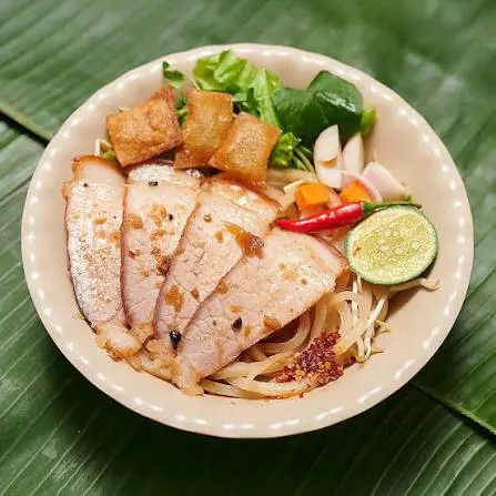 Tô cao lầu xếp lát thịt xá xíu, ram chiên giòn, rau sống, ớt và tắc tươi trên nền lá chuối xanh