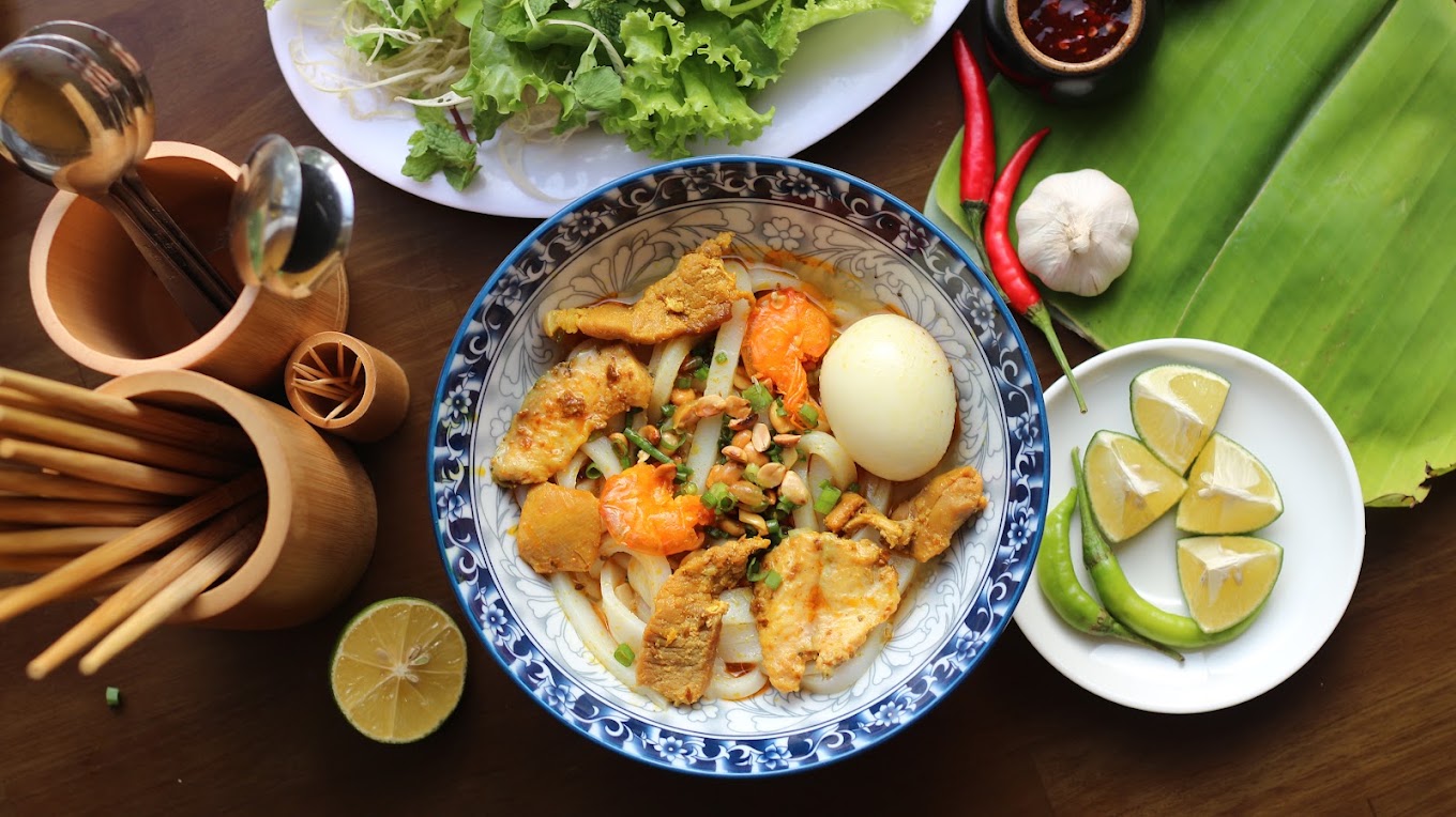 Tô Mì Quảng Đà Nẵng với tôm, thịt, trứng luộc, đậu phụng cùng dĩa rau sống và chanh ớt tươi trên bàn gỗ
