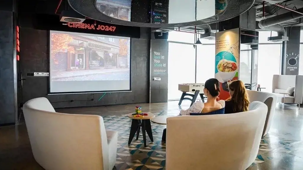 Không gian sinh hoạt chung và giải trí hiện đại tại Tru by Hilton Da Nang City Centre, thành phố Đà Nẵng. Căn phòng được trang bị màn hình chiếu phim khổ lớn, sofa thư giãn, bàn chơi bi-lắc và cửa kính rộng đón ánh sáng tự nhiên ban ngày, tạo không gian thoải mái cho khách lưu trú.