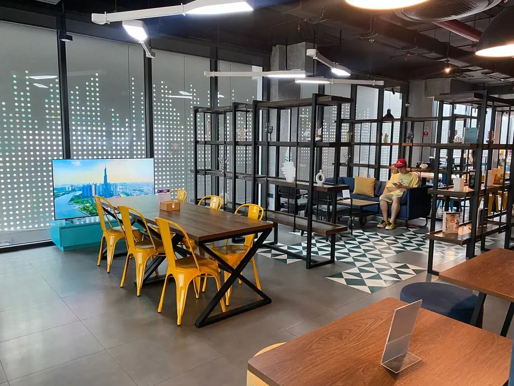 Khu vực làm việc và sảnh nghỉ ngơi hiện đại với bàn gỗ, ghế màu vàng tươi và kệ trang trí tại khách sạn Tru by Hilton Da Nang City Centre – Thiết kế trẻ, không khí thoải mái