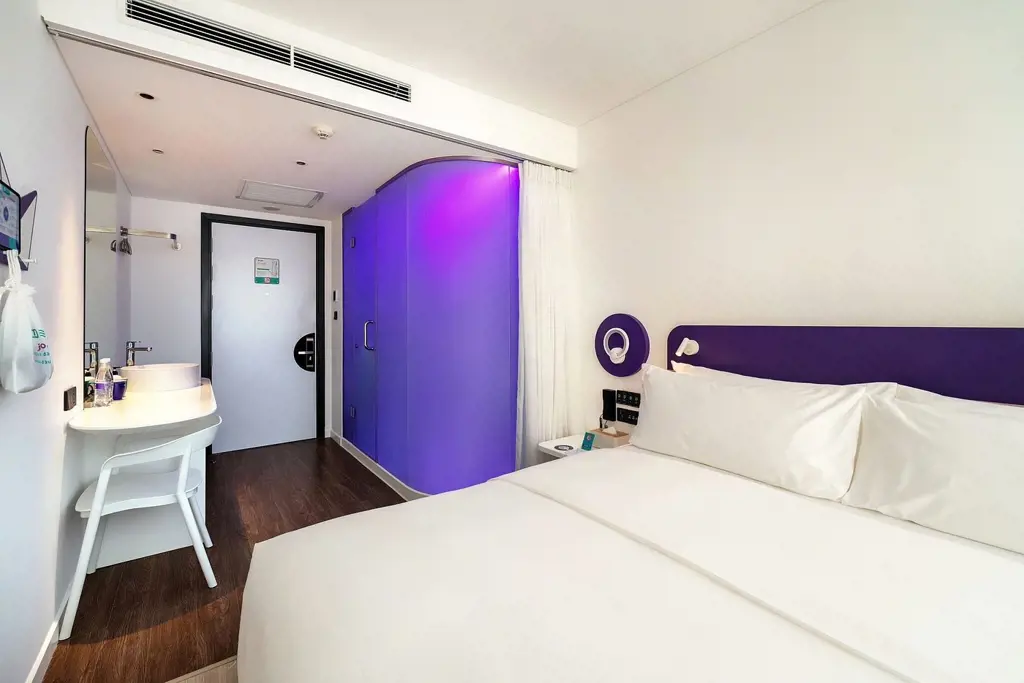 Không gian phòng nghỉ hiện đại tại khách sạn Tru by Hilton Da Nang City Centre với giường đôi trắng và buồng tắm kính phát sáng sắc tím. – Phòng King