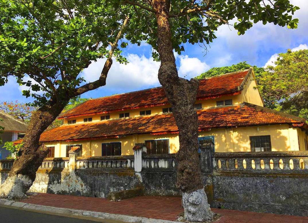Dinh Chúa Đảo ở Côn Đảo - Mặt tiền tòa nhà cổ mái ngói đỏ, tường vàng nhạt và hàng cây lớn phía trước. – Hành trình khám phá lịch sử tại Côn Đảo