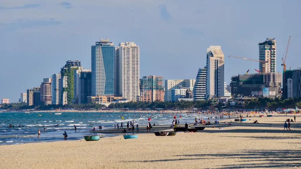 Bãi biển Mỹ Khê Đà Nẵng đông đúc với nhiều người tắm biển và các tòa nhà cao tầng hiện đại phía sau.
