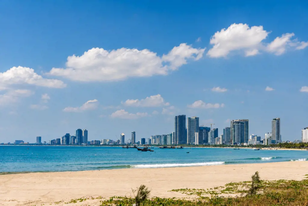 Bãi biển Mỹ Khê cát vàng, nước biển xanh ngọc và đường chân trời thành phố Đà Nẵng với các tòa nhà cao tầng dưới bầu trời xanh mây trắng.