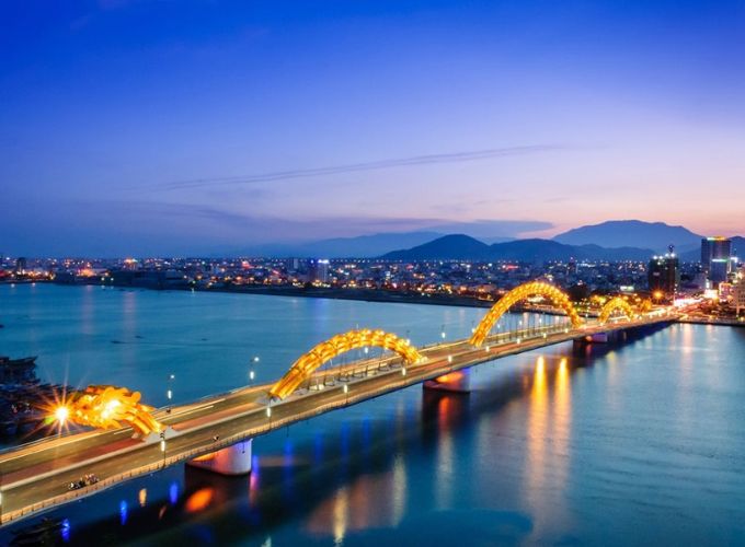 Cầu Rồng ở Đà Nẵng rực rỡ ánh đèn vàng cam vào buổi tối, bắc qua sông Hàn với thành phố lung linh phía sau.