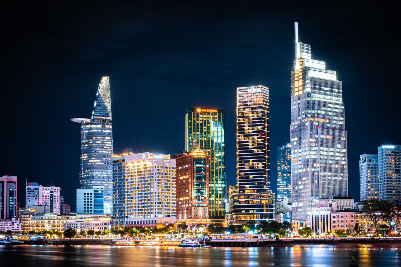 Illuminated skyscrapers along the Saigon River in Ho Chi Minh City at night, including the Bitexco Financial Tower and Vietcombank Tower.