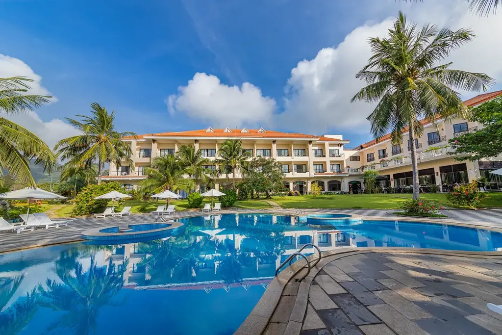 Hồ bơi ngoài trời trong xanh phản chiếu bóng tòa nhà và rặng dừa tại Côn Đảo Resort – Điểm khác biệt nổi bật của Côn Đảo Resort