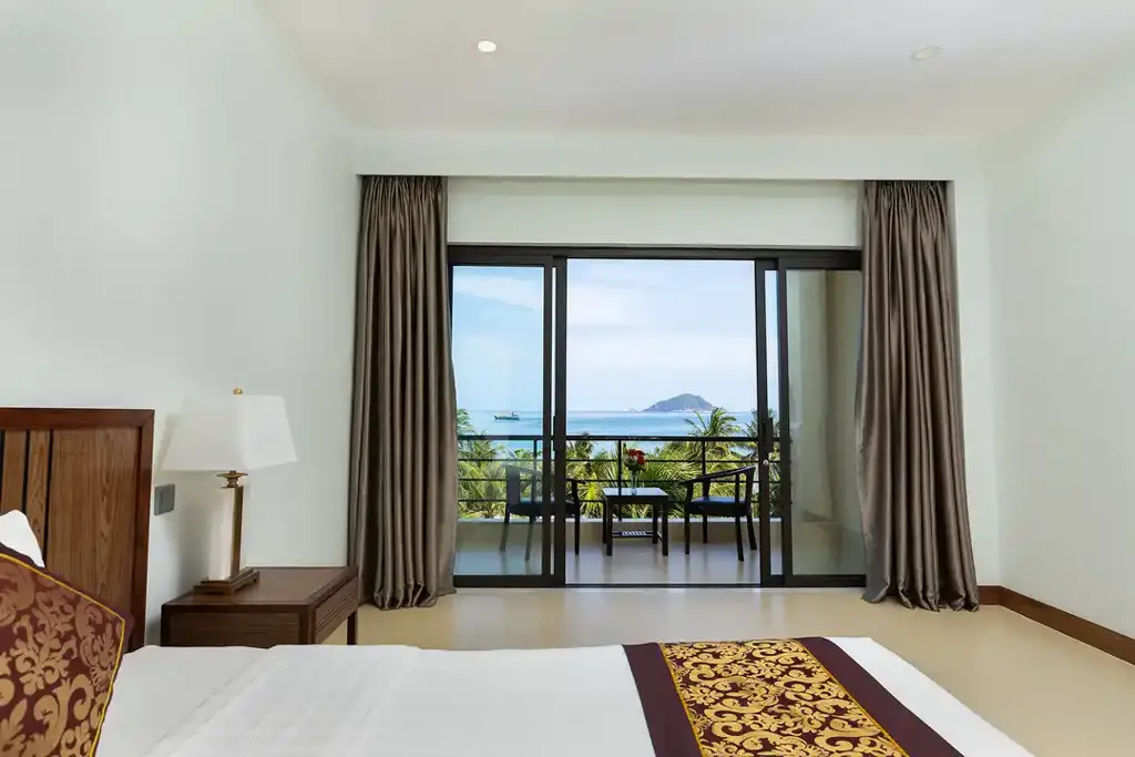 Phòng Deluxe tại resort với giường lớn, cửa kính mở ra ban công có bàn ghế và tầm nhìn hướng biển.
